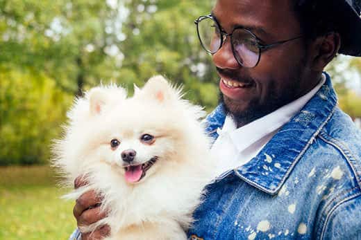 African-American man holding pomeranian at the park.