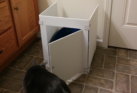 Gray cat sniffing cardboard cat litter box stall.