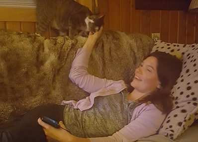 Woman lying on couch pets cat standing above her.