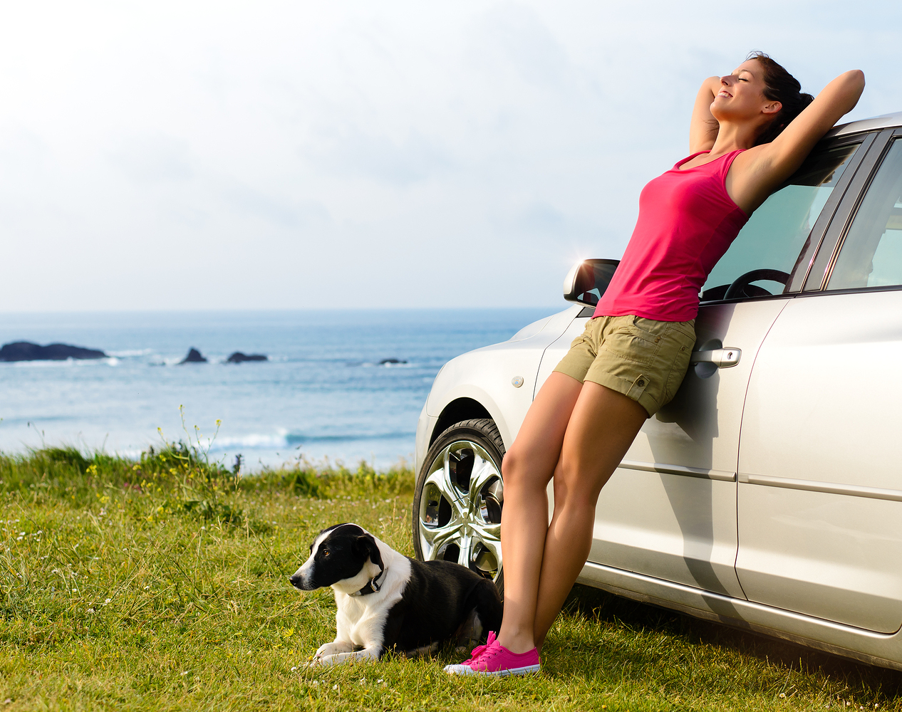 Dog lies next to a woman leaning on a car.