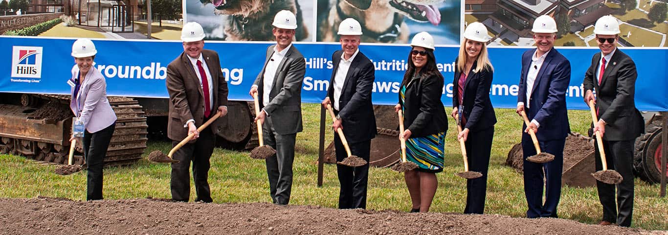 Group of people wearing hard hats with shovels at a groundbreaking ceremony for Hill's Pet Nutrition.